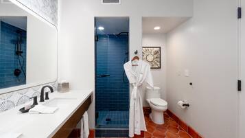 A bathroom with a white sink, a mirror, a towel, a white toilet, and a blue shower enclosure.