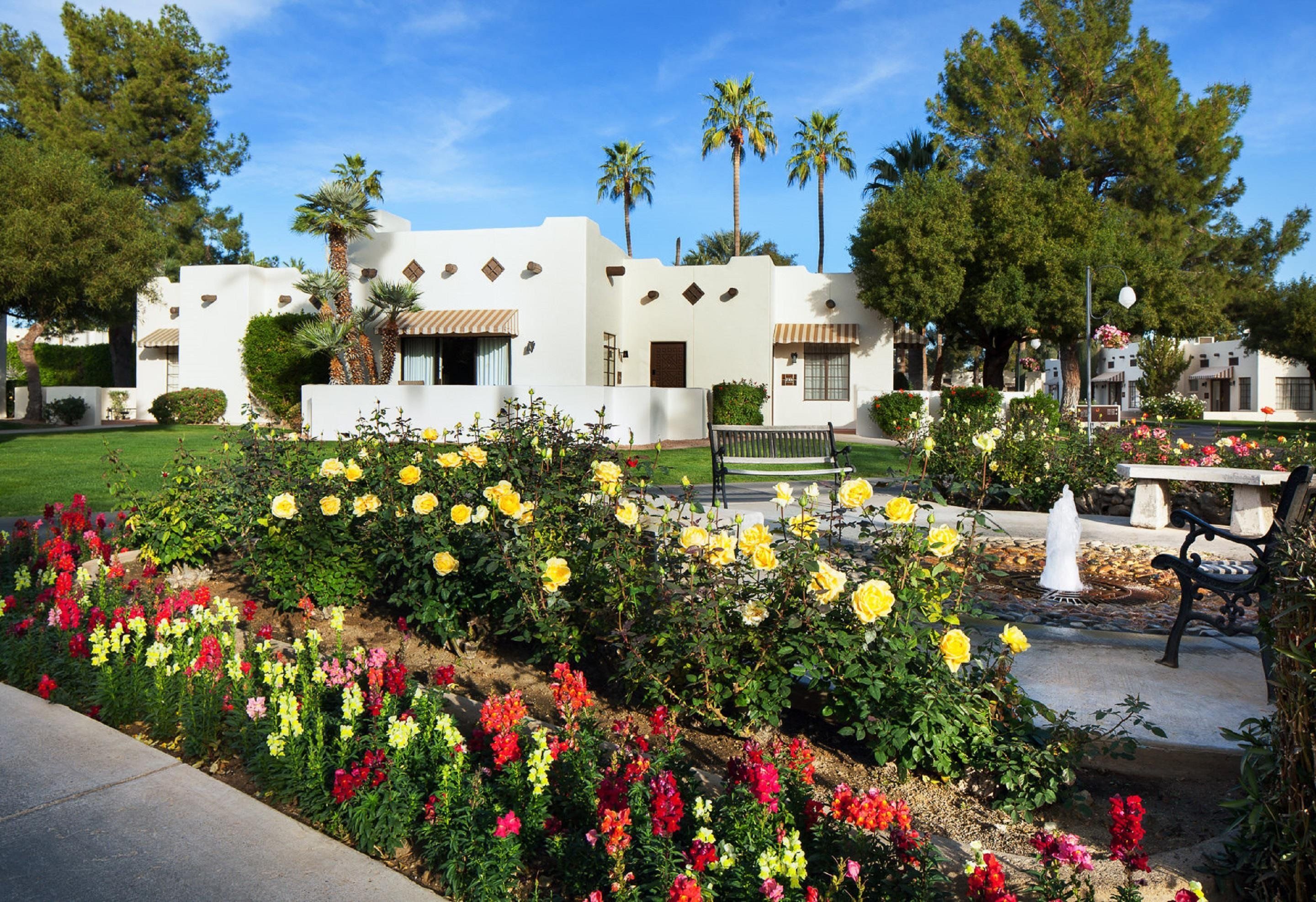Ein Gebäude mit weißer Fassade, zahlreichen Fenstern und einem Garten mit gelben und roten Blumen.