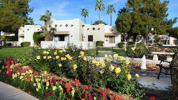 Ein Gebäude mit weißer Fassade, zahlreichen Fenstern und einem Garten mit gelben und roten Blumen.