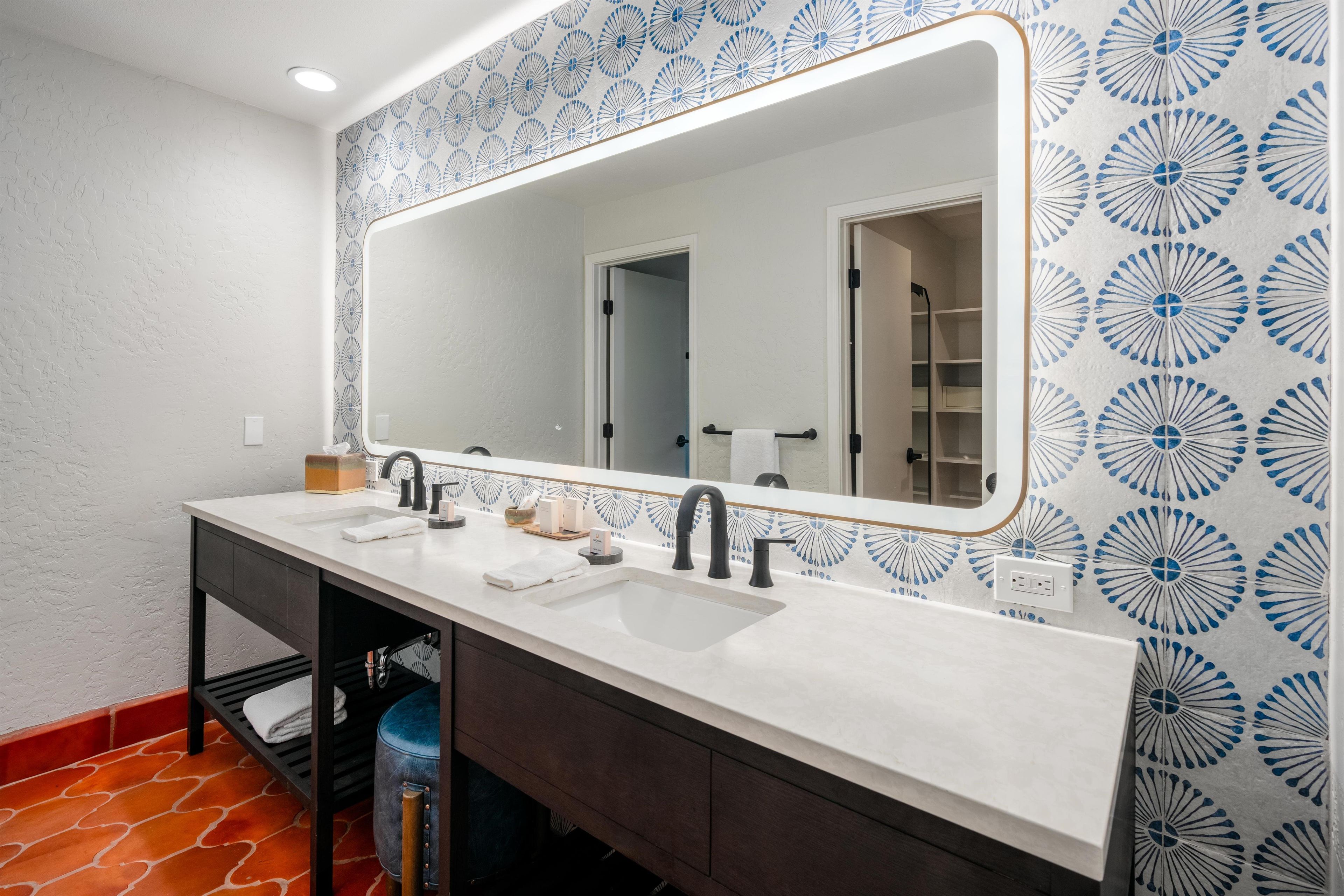 A bathroom with a double sink vanity, a large mirror, and patterned wall tiles.
