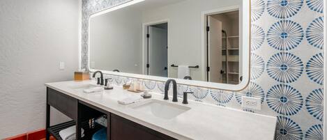 A bathroom with a double sink vanity, a large mirror, and patterned wall tiles.