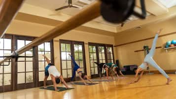 A yoga class in a room with large windows, wooden floors, and exercise equipment.