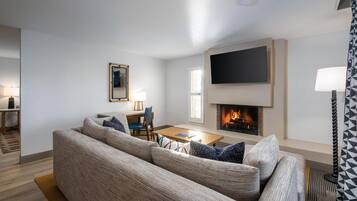 A living room with a sofa set, a flat-screen TV, a fireplace, and a dining area.