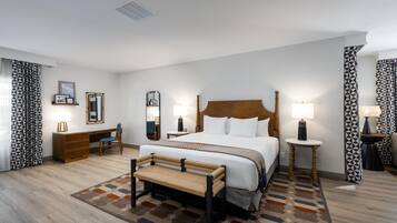 A hotel room with a large bed, bedside tables, a desk, a chair, and patterned curtains.