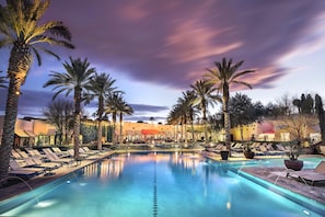 A pool area with lounge chairs and palm trees, surrounded by buildings with warm lighting. - The Wigwam (Litchfield Park)