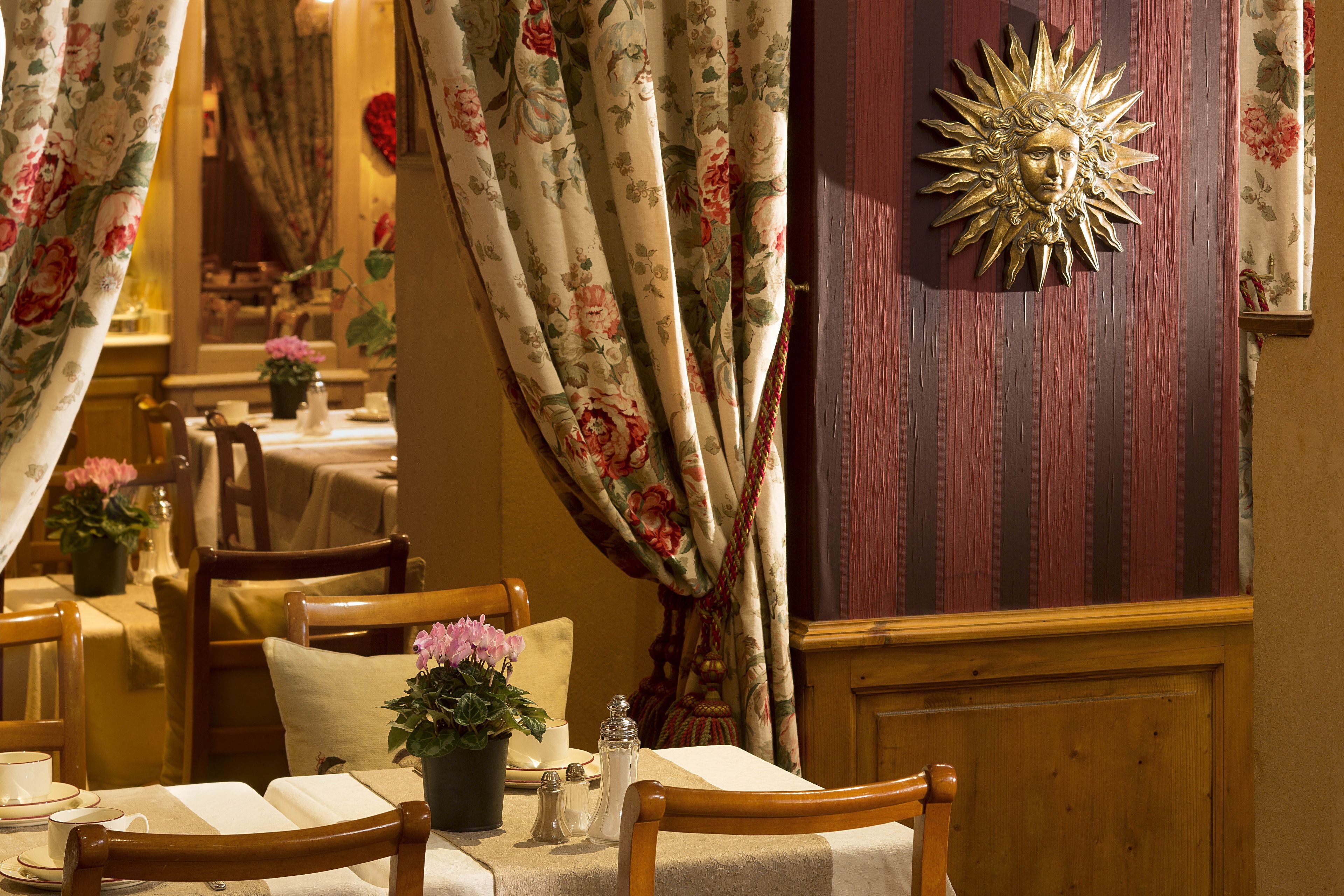 A dining area with wooden chairs, tables, and floral curtains.
