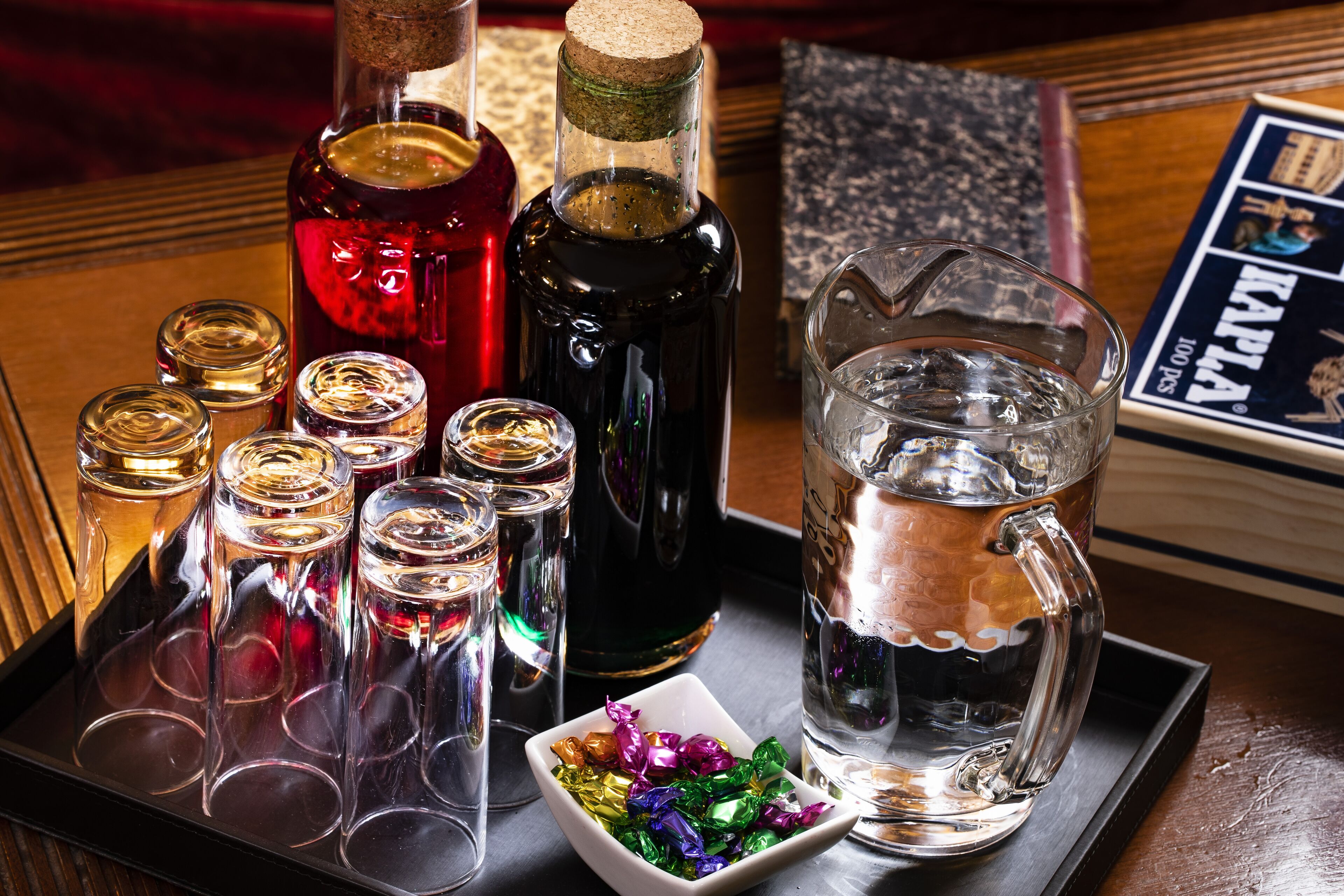 A tray with various bottles and glasses, a pitcher, and a small bowl of colorful items.