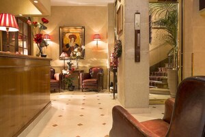 A lobby with a reception desk, leather chairs, a large painting, and a staircase.