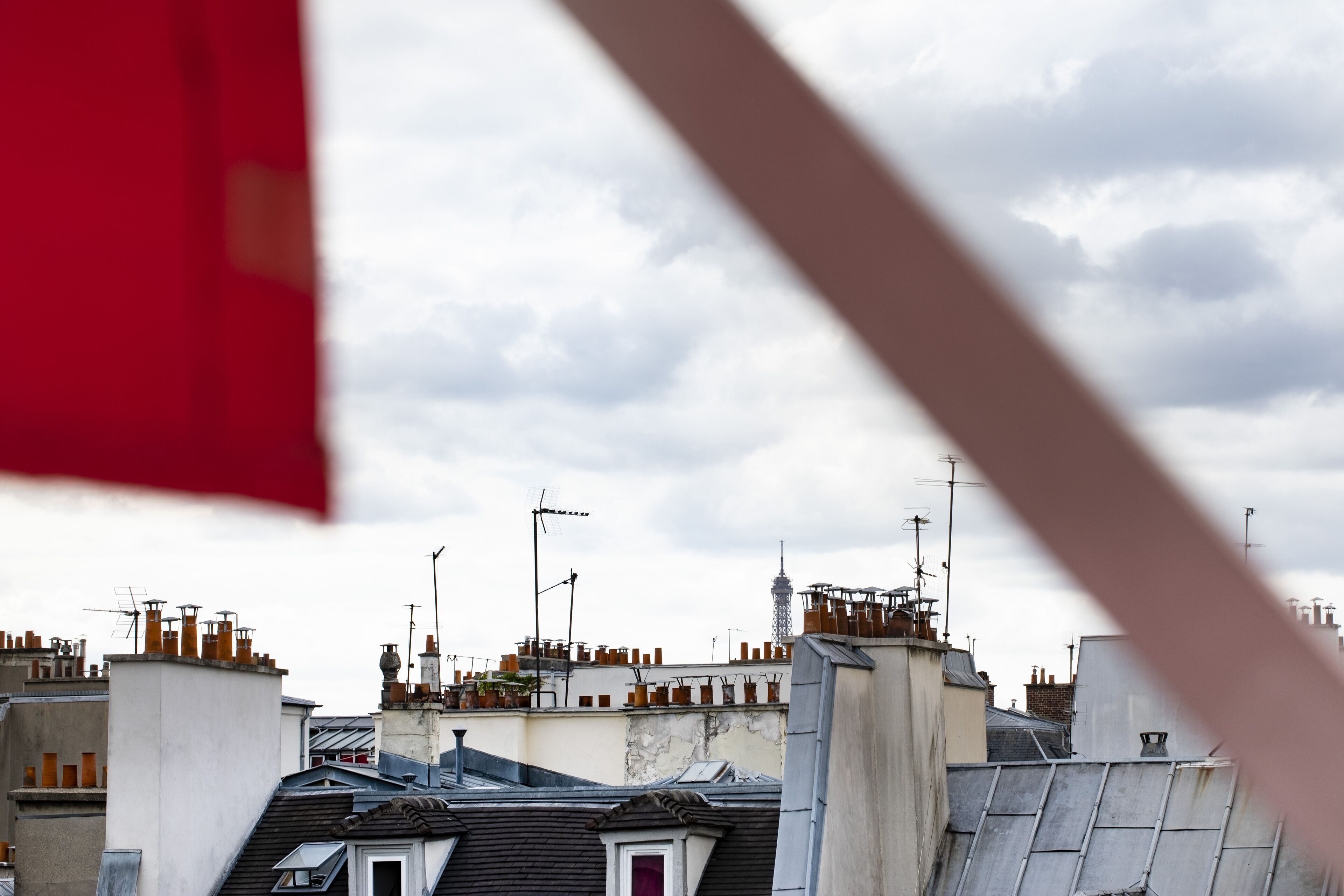 A view of rooftops with multiple chimneys and antennas, under a cloudy sky.