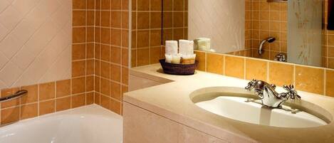A bathroom with a bathtub, a sink, and a mirror. There is a towel rack on the wall and a basket with toiletries on the counter.