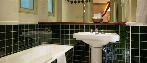 A bathroom with a white bathtub, a white sink, and green-tiled walls.