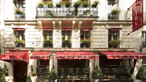 Fachada de hotel com toldo vermelho, várias varandas com plantas em vasos e uma placa com a inscrição 'HOTEL BRITANNIQUE'.