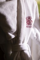 Un accappatoio bianco con logo e scritta ricamati in rosso.