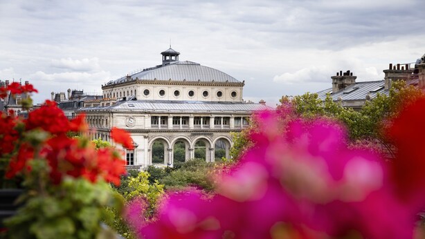 Um edifício histórico com cúpula e janelas em arco, rodeado por vegetação exuberante e flores vibrantes.