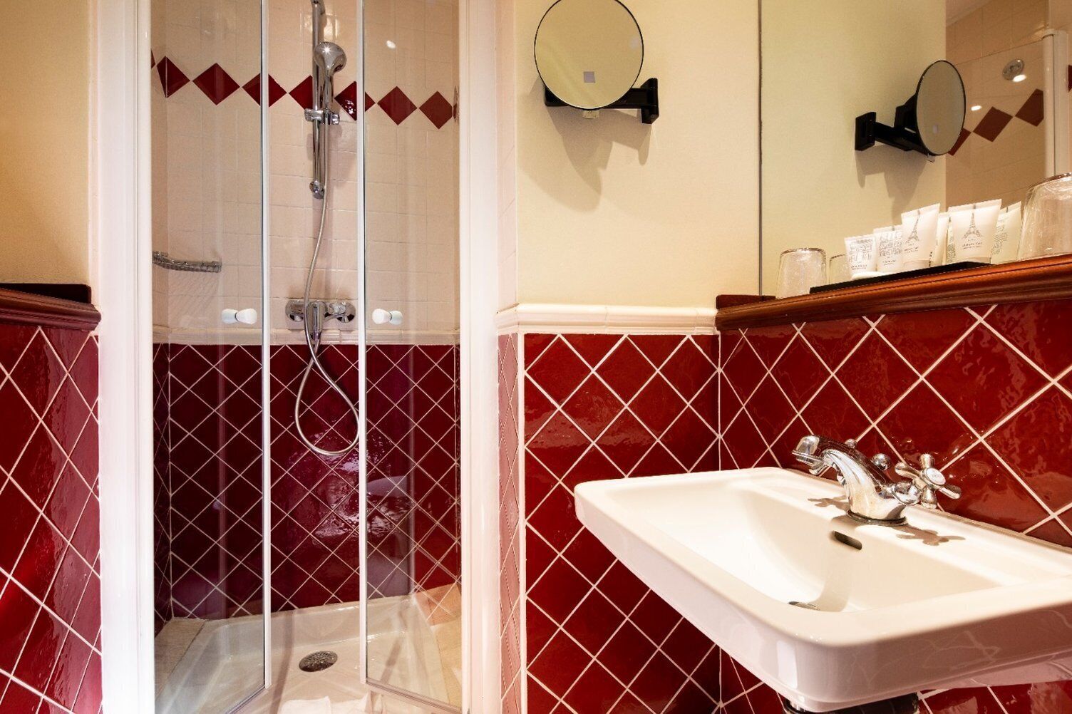 Un baño con cabina de ducha de vidrio, un lavabo con espejo y paredes con azulejos rojos.