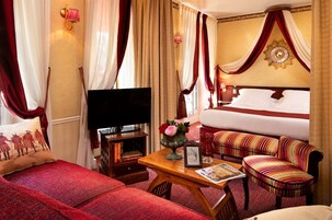 Cómoda habitación de hotel con cama, sofá, televisión y una pequeña mesa con un jarrón de flores.