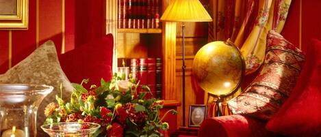 Um quarto aconchegante com um sofá vermelho, uma estante de madeira, um globo e velas.