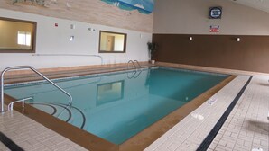 An indoor swimming pool with clear water, a lifeguard sign, and a mural of a beach scene on the wall.