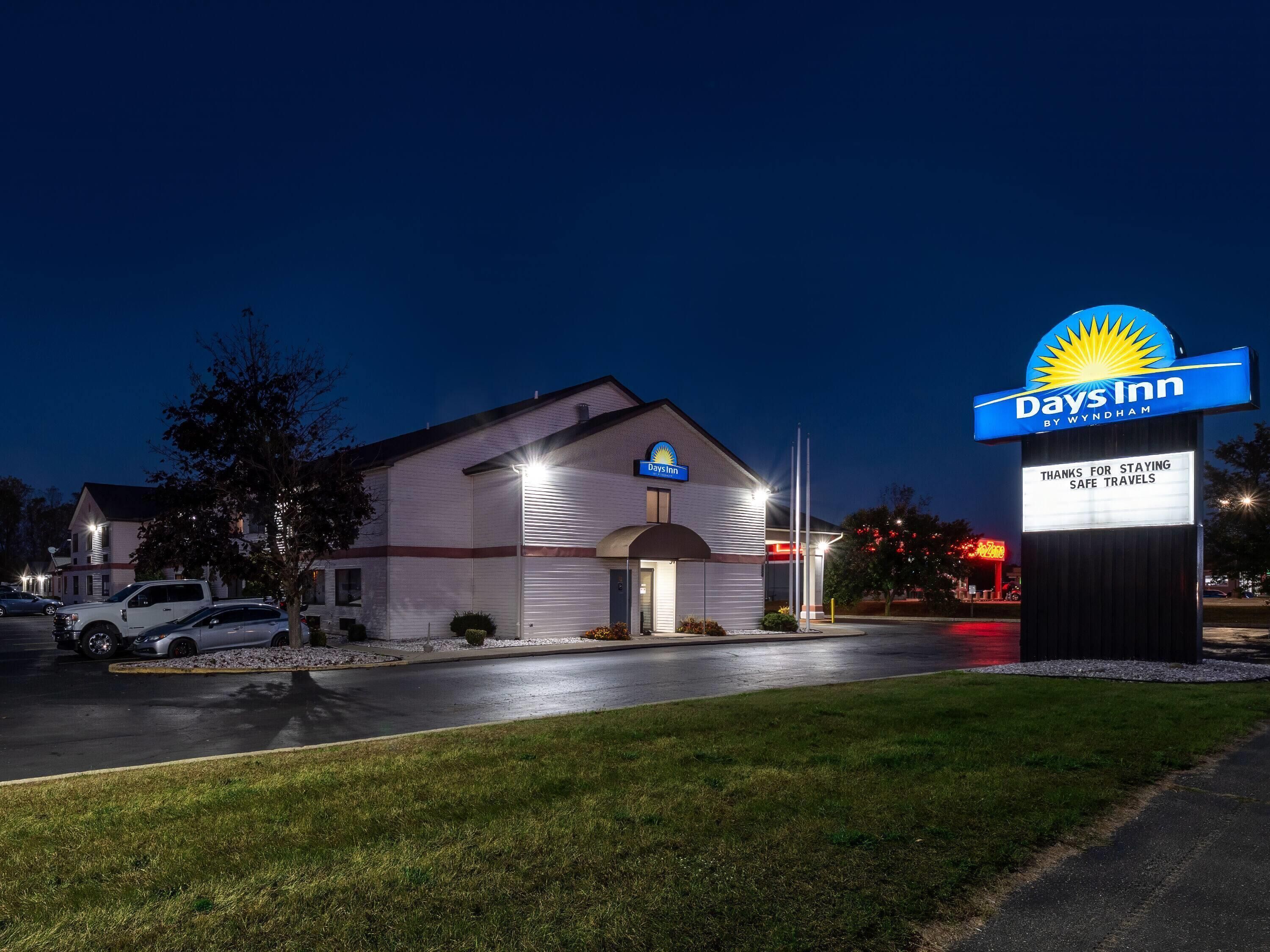 Un Days Inn by Wyndham con insegna, parcheggio e facciata dell'edificio ben illuminata.