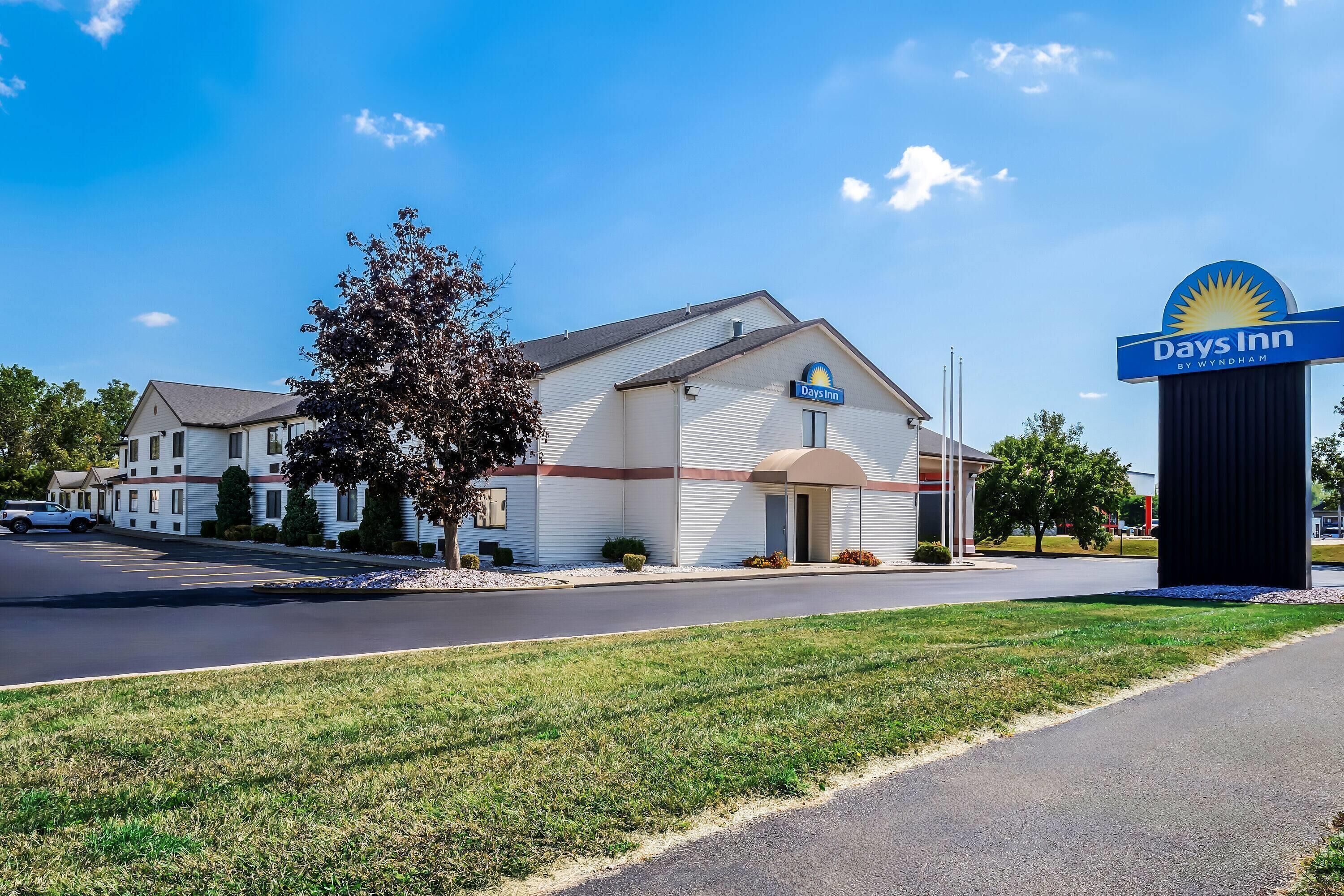 A Days Inn by Wyndham hotel with a clear sky, a parking lot, and a grassy area in front.