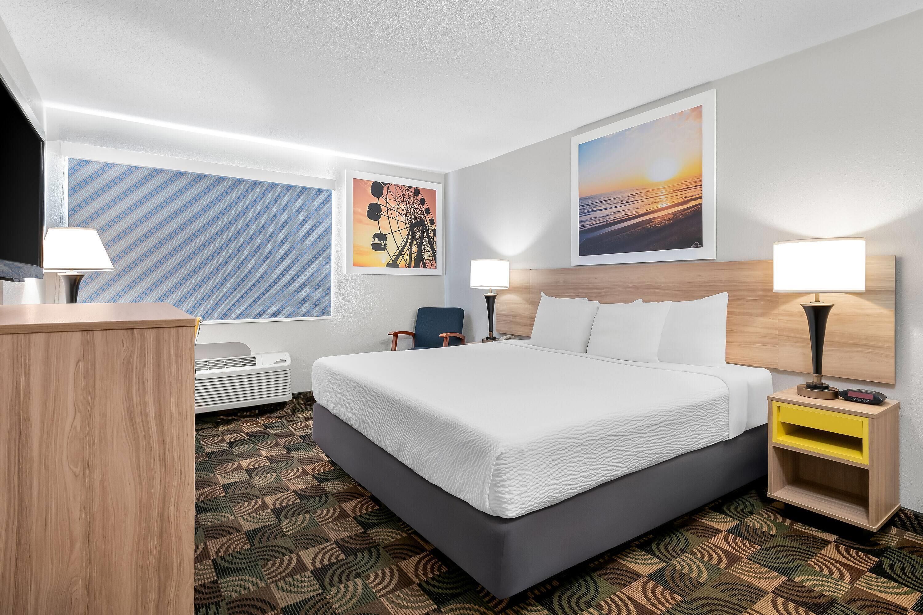 Una habitación de hotel con una cama grande, un escritorio, una silla, una mesita de noche con lámpara y un televisor montado en la pared.