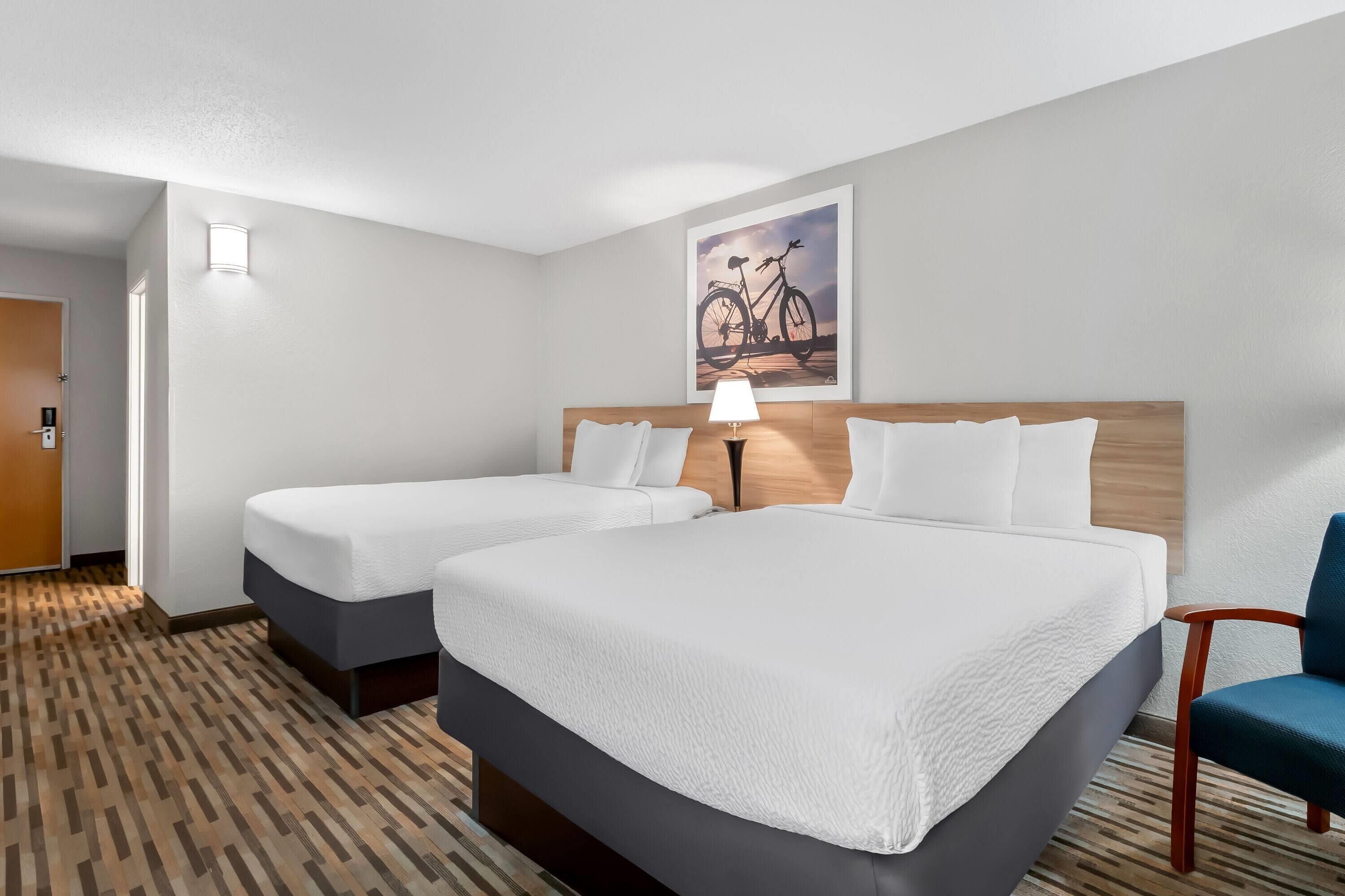 A hotel room with two beds, a wooden headboard, a lamp, and a wall-mounted picture of a bicycle.