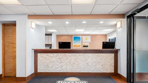 A reception area with a reception desk, two monitors, framed artwork, and a Days Inn Hillsdale logo on the floor mat.