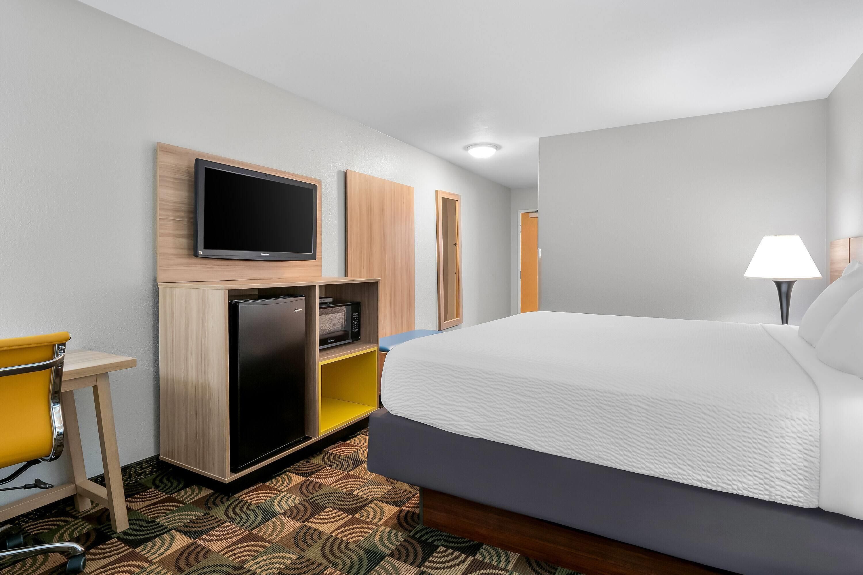 Una habitación de hotel con cama, escritorio, televisión, microondas y lámpara.