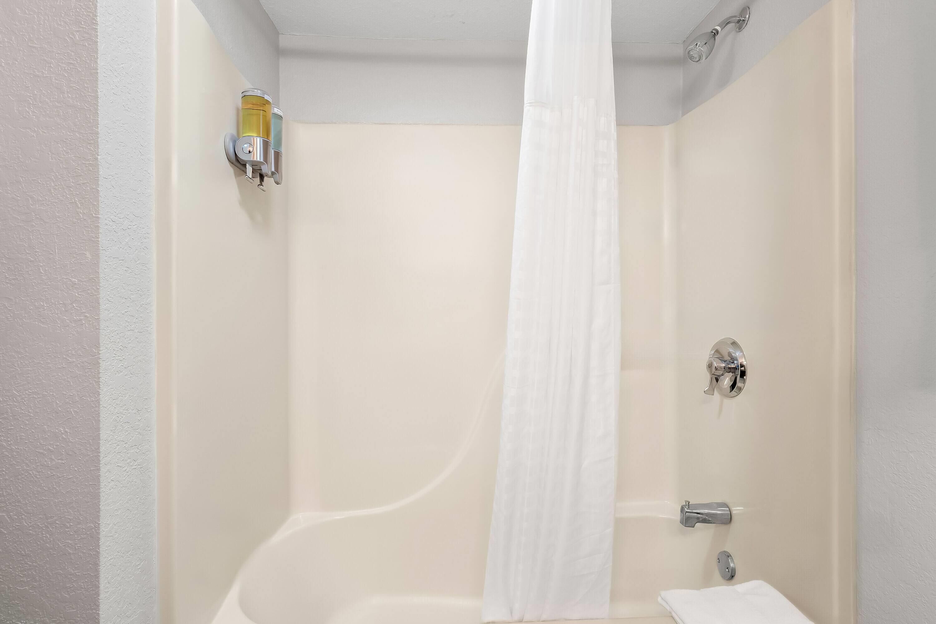 Un baño con bañera, cortina de ducha, toallero y dispensador de jabón.