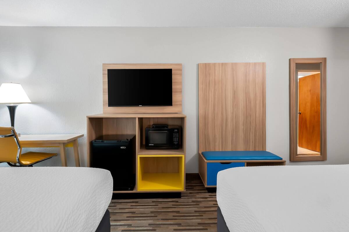 Habitació d'hotel amb llit, escriptori amb làmpada, televisió, microones, maleta i armari.