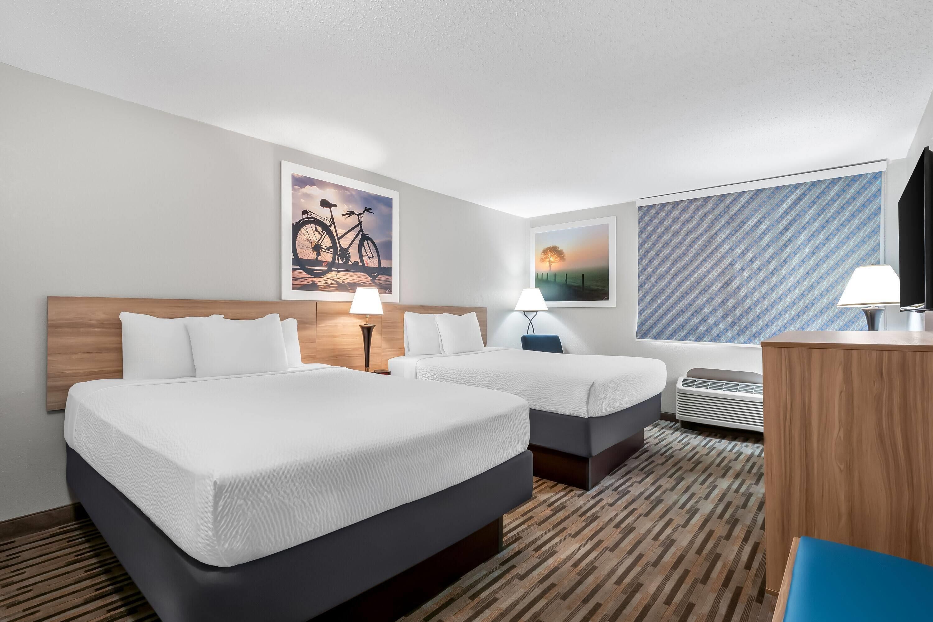 A hotel room with two beds, a desk, a TV, and artwork on the walls.