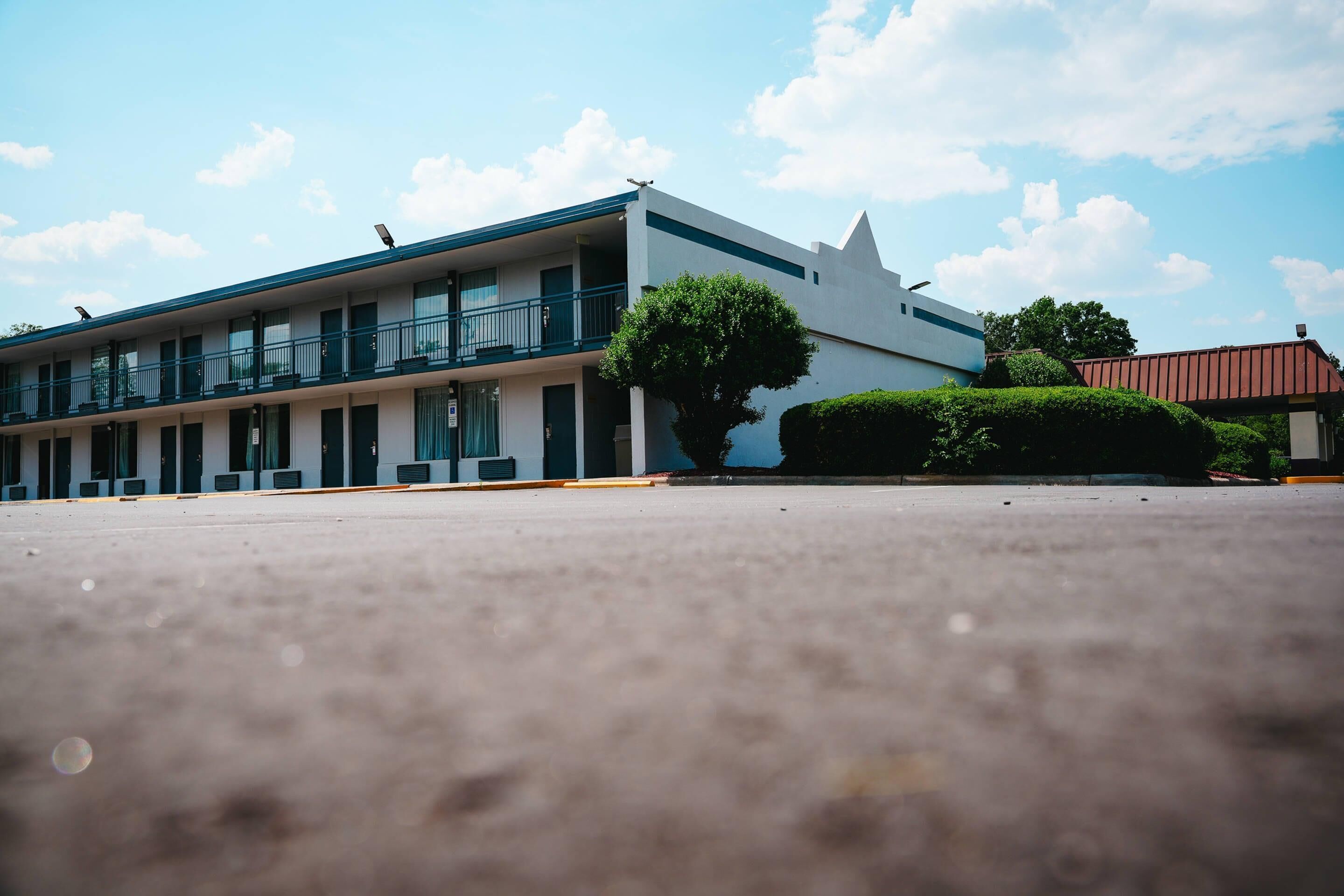 A motel with a row of rooms, a covered parking area, and a tree in the foreground.