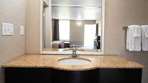 A bathroom with a granite countertop, a sink, a mirror, and a towel rack with towels. - Rodeway Inn Monroe (Monroe)