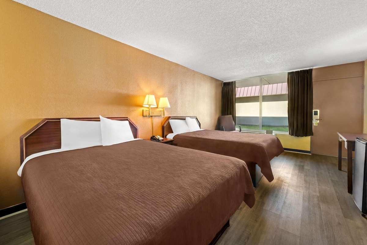 A hotel room with two beds, a desk, a chair, and a window with curtains.