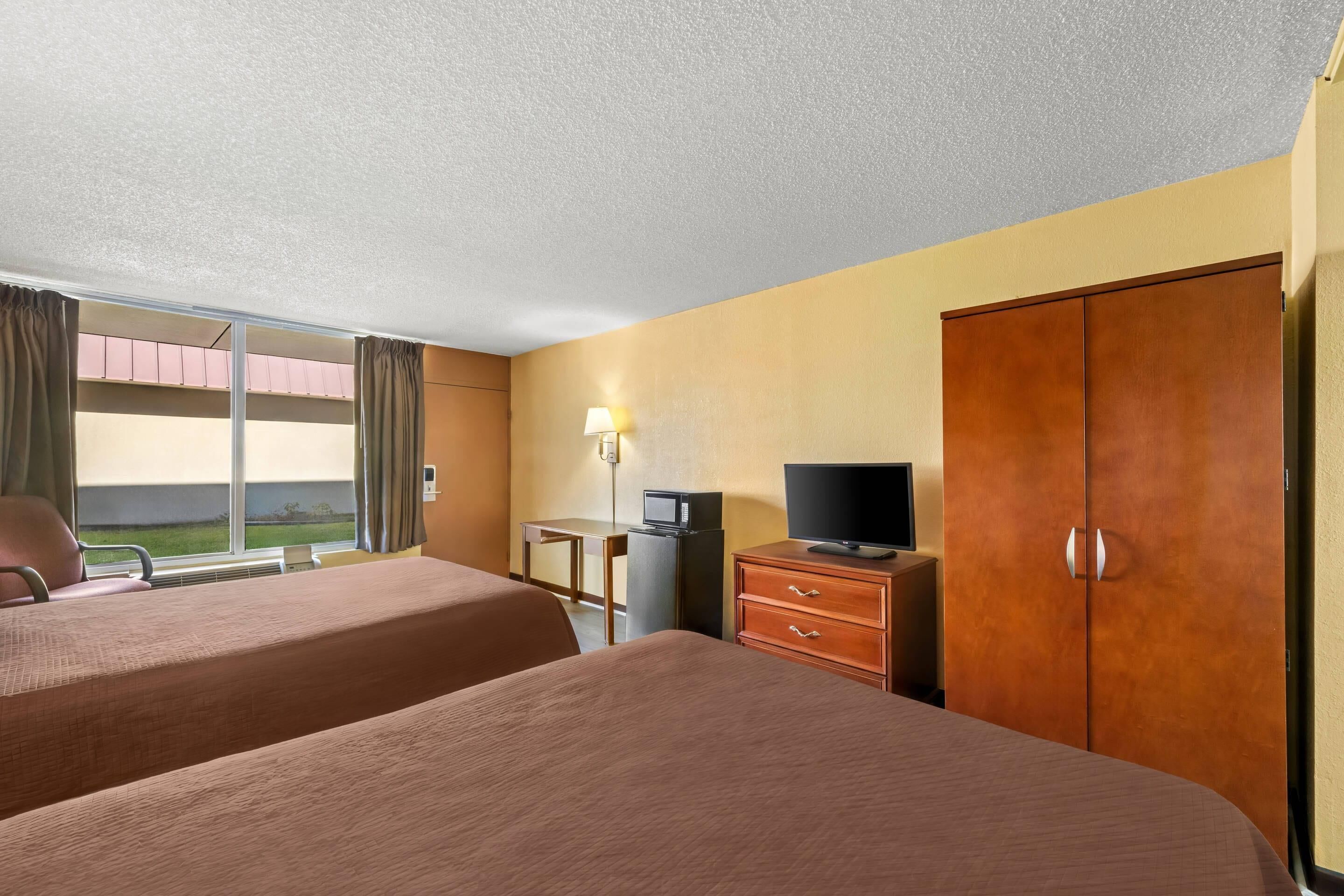 Una habitación de hotel con dos camas, televisión, escritorio con lámpara y armario.
