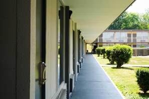 A covered corridor with a row of windows, a concrete walkway, and a building in the background.