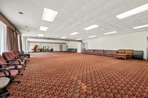 Un amplio salón de conferencias con alfombra estampada, filas de sillas, una zona de sofás y una mesa.