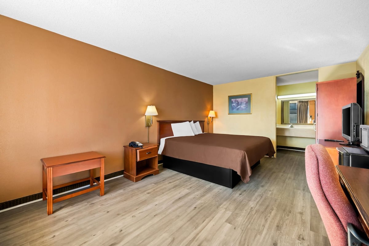 A hotel room with a bed, bedside table, lamp, TV, and a small desk.