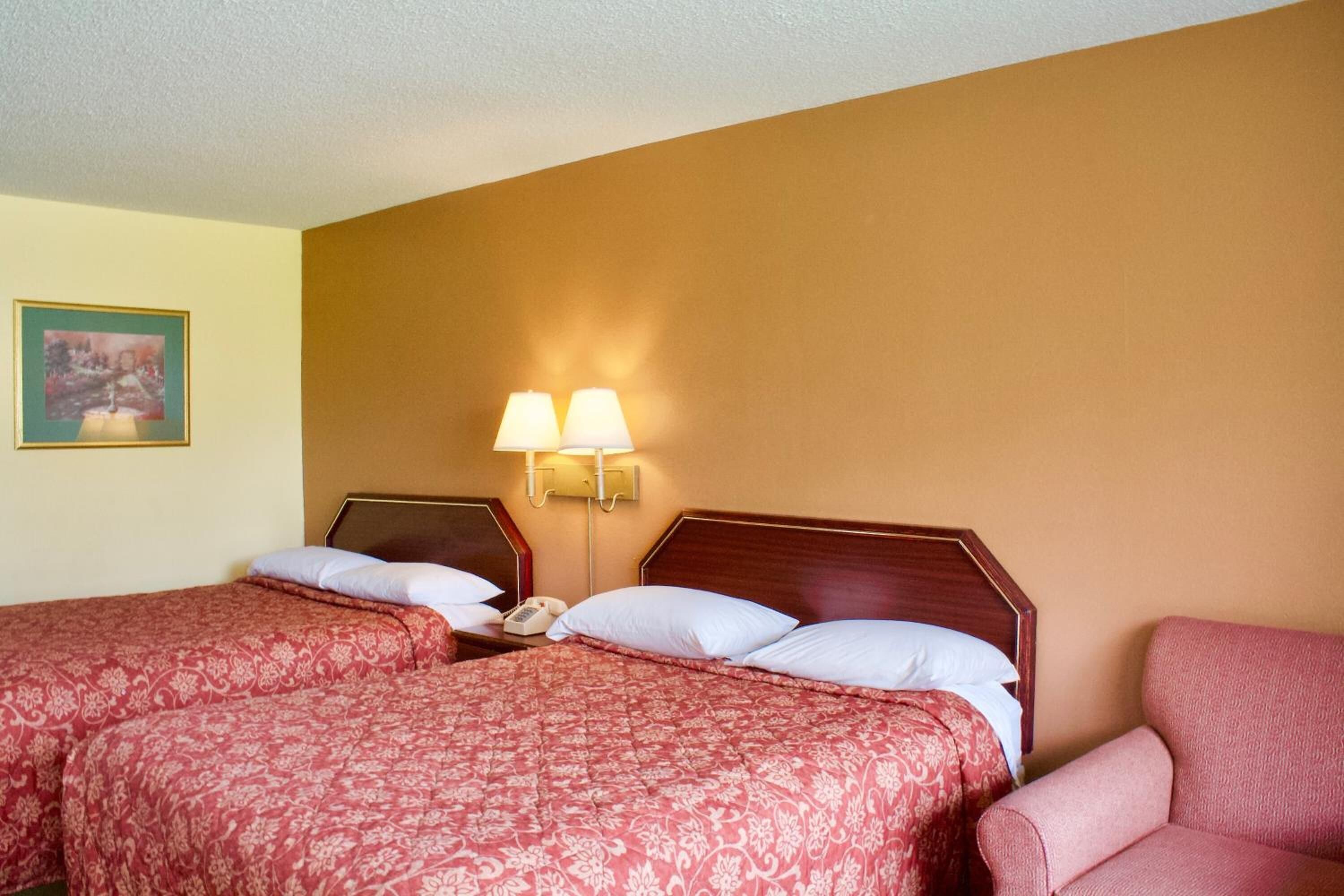 A hotel room with two beds, each with a wooden headboard, a bedside lamp, and a telephone.