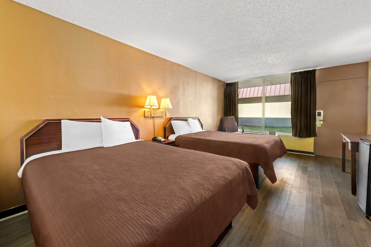 A hotel room with two beds, a desk, a chair, and a window with curtains.