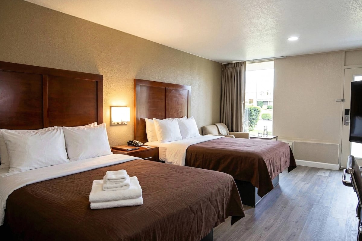 A hotel room with two beds, a desk, a chair, a TV, and a window with curtains.