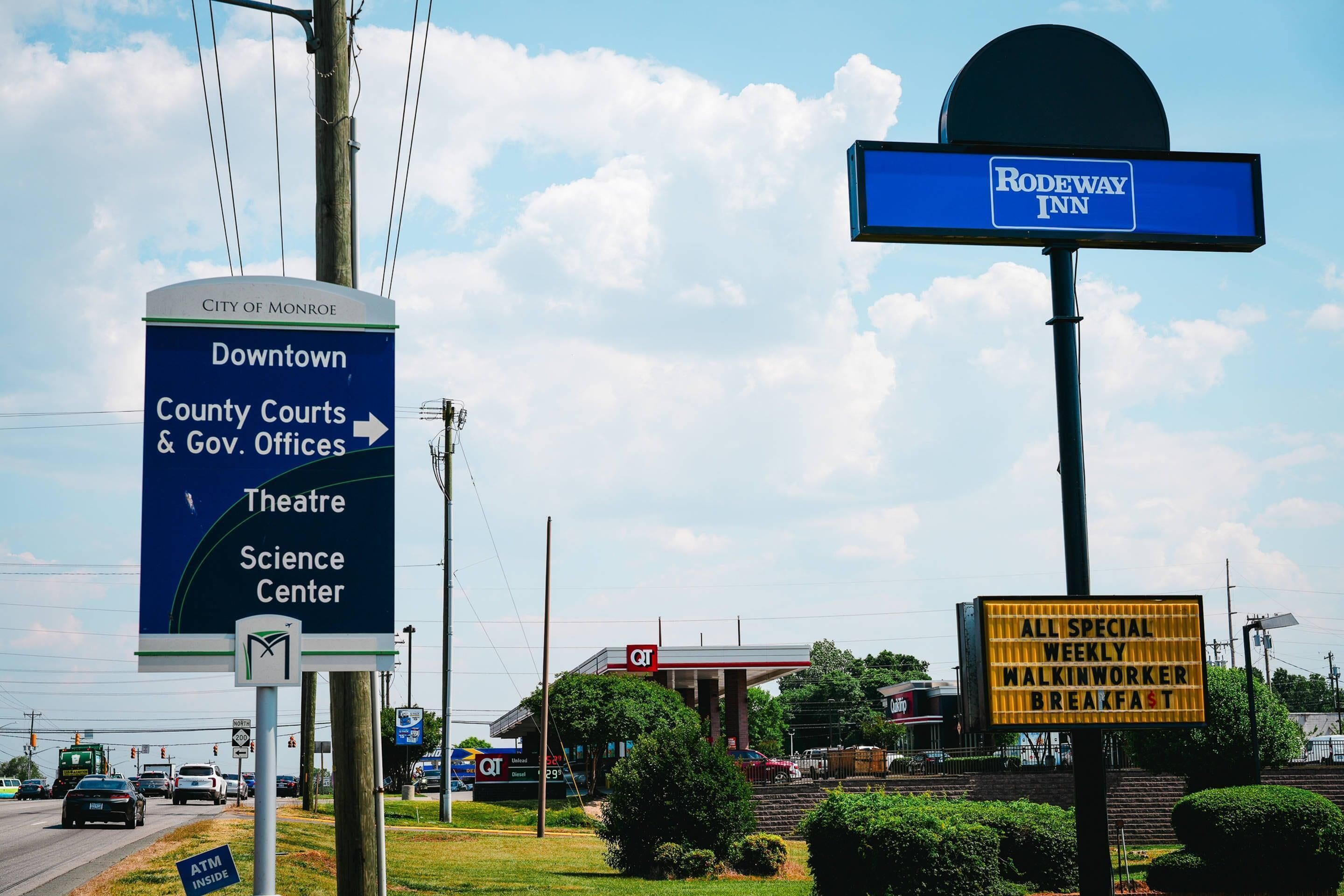A sign for the Rodeway Inn, a sign for the City of Monroe Downtown, and a sign for AT&T services.