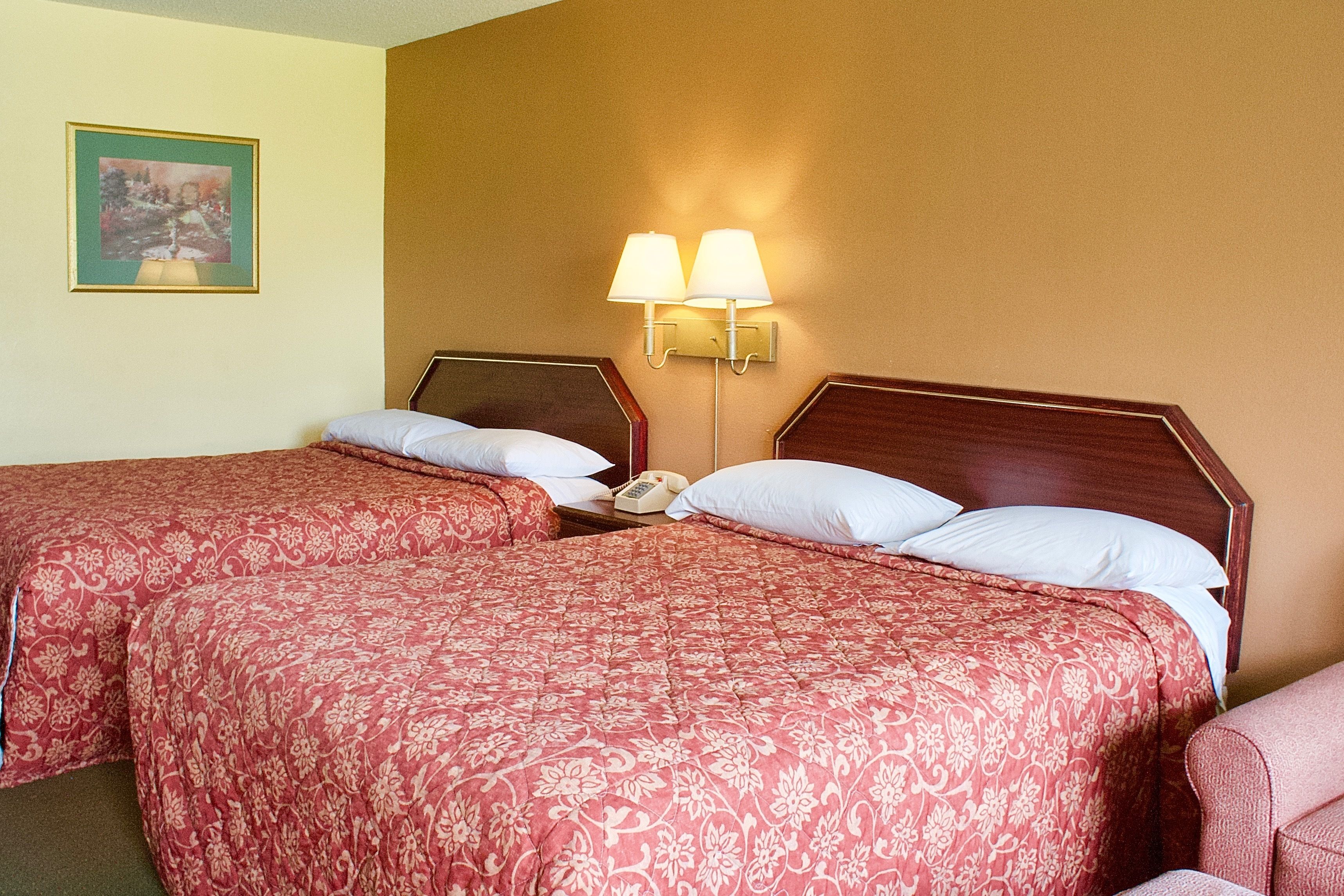 A hotel room with two beds, each with a red floral bedspread, a wooden headboard, and a nightstand with a telephone.