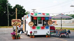 A taco truck parked in a lot with a sign reading 'Taco loco,' tables with colorful blankets, and potted plants. - Rodeway Inn Monroe (Monroe)