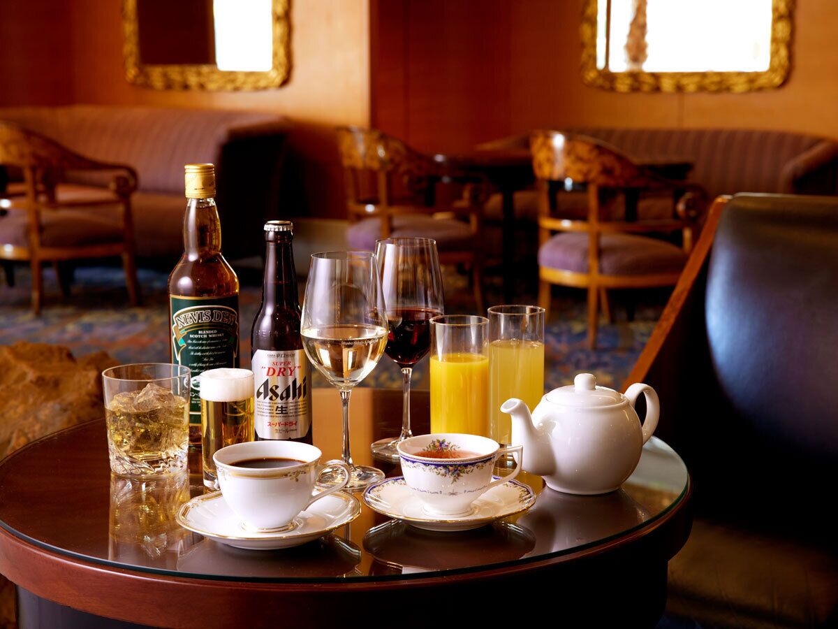 A dining table set with a bottle of whiskey, glasses, a teapot, and a cup of coffee.