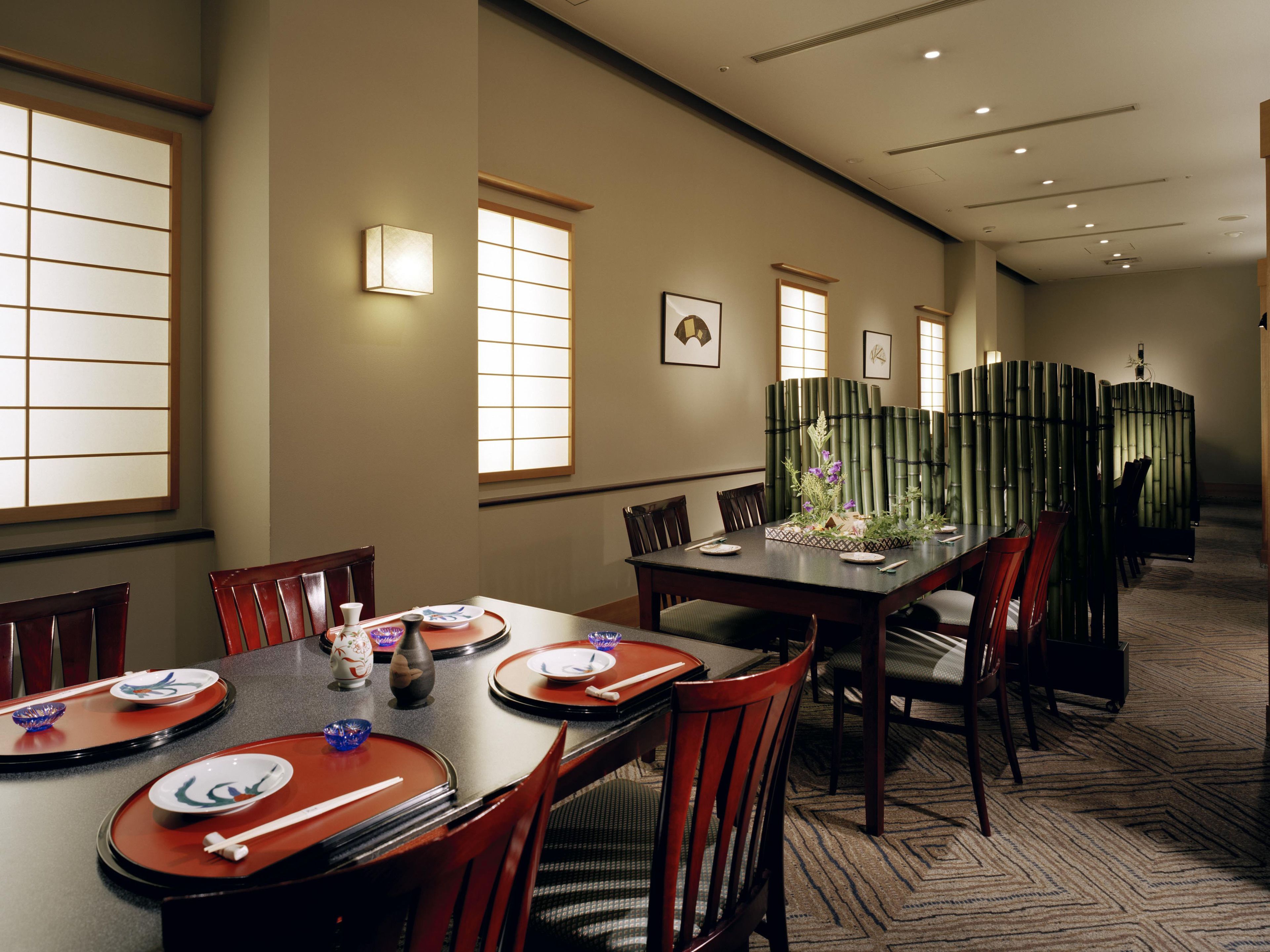 A dining area with a long table, chairs, and a bamboo partition.