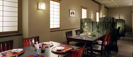 A dining area with a long table, chairs, and a bamboo partition.