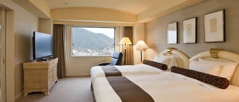 A hotel room with a large bed, a TV on a dresser, a window with a mountain view, and a lamp.