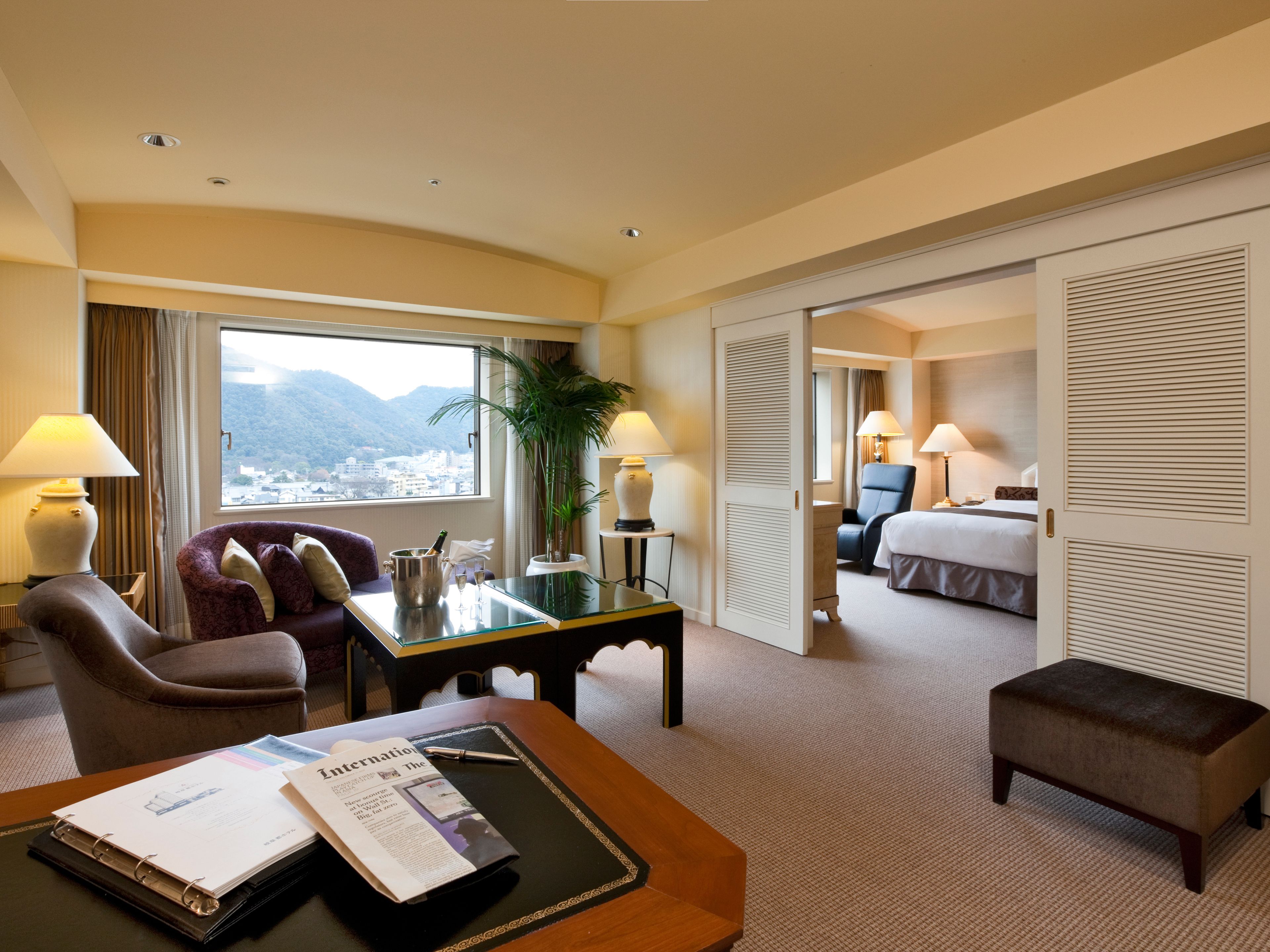 A hotel room with a desk, chair, and a bed. There is a window with a view of mountains.