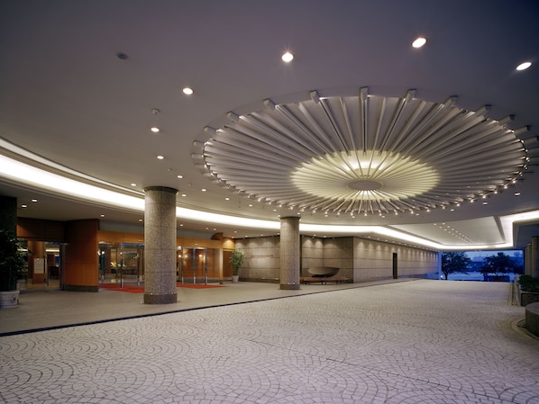 Un hall d’entrée spacieux, doté d’un plafond au design moderne, de grandes colonnes et d’un revêtement de sol à motifs.